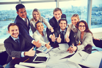 Group of business partners showing thumbs up while sitting at workplace in office